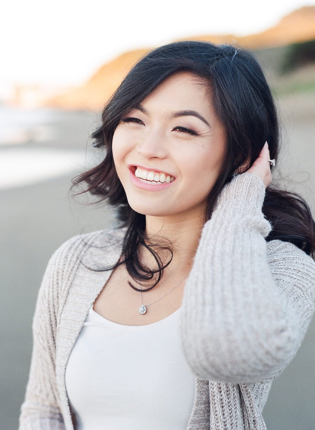 Ethnically Asian lady with black hair wearing a pendant smiles and poses at the beach.