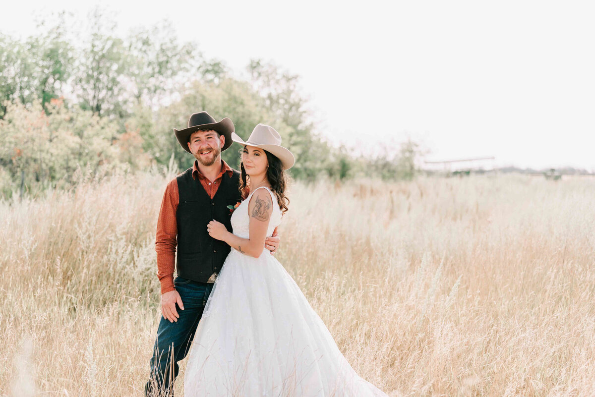 Bride and groom stand together side by side in the field. 