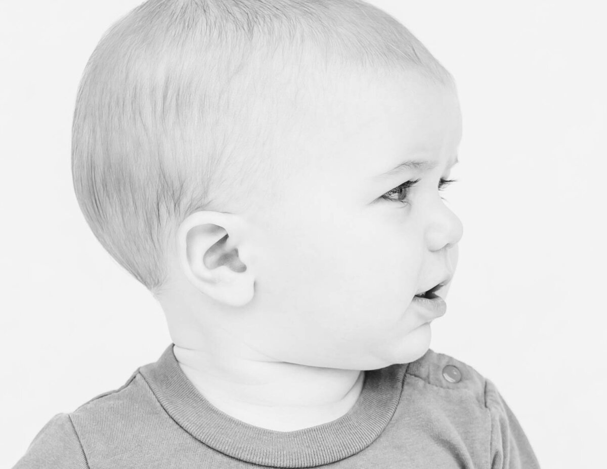 Black and white fine art portrait of baby boy on white backdrop capturing sweet innocence