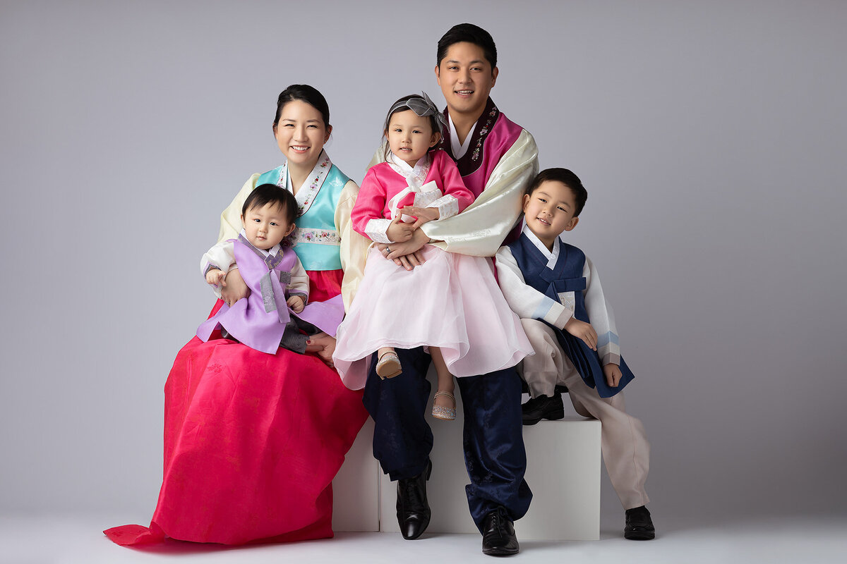 A family wearing traditional Korean Hanbok attire, beautifully captured by a Dallas family photographer, highlighting their cultural heritage in a timeless studio portrait.