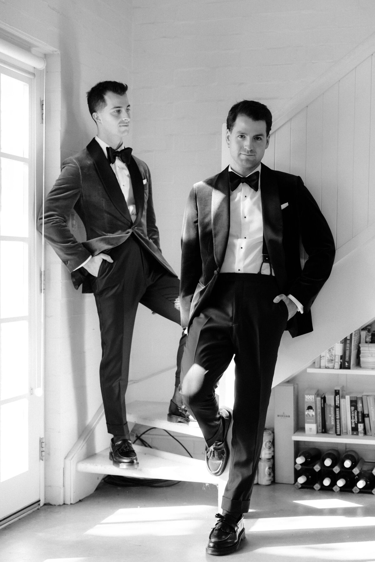 Black and white image of two grooms posing at the bottom of a staircase.