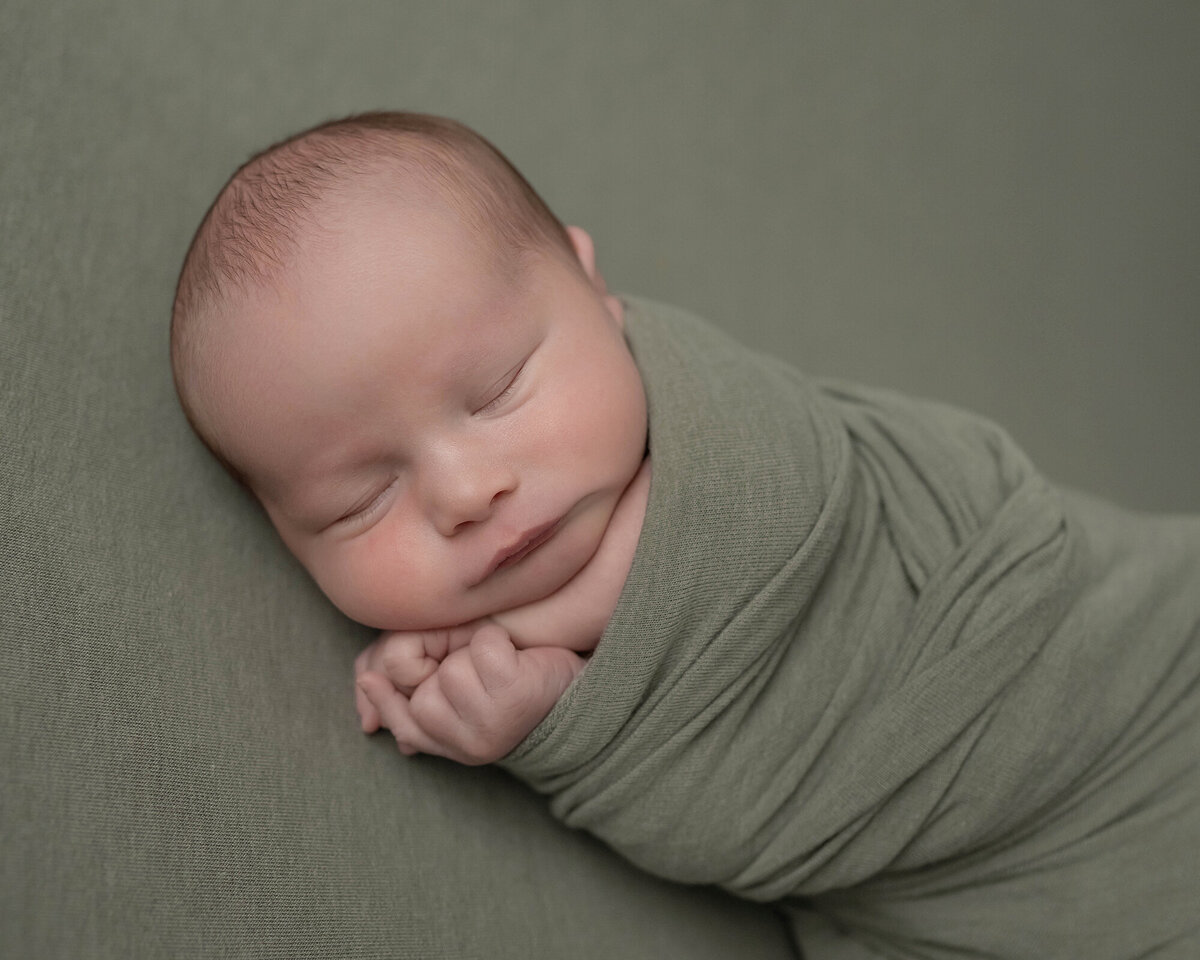 A side sleeping newborn in a tight green swaddle with hands poking out