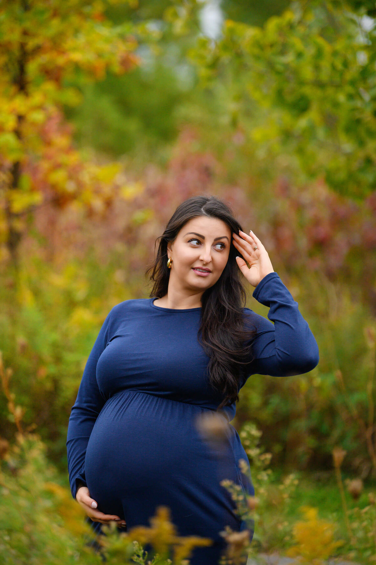 pregnant woman with her hand in her hair wearing a blue maternity dress for her fall outdoor maternity photos