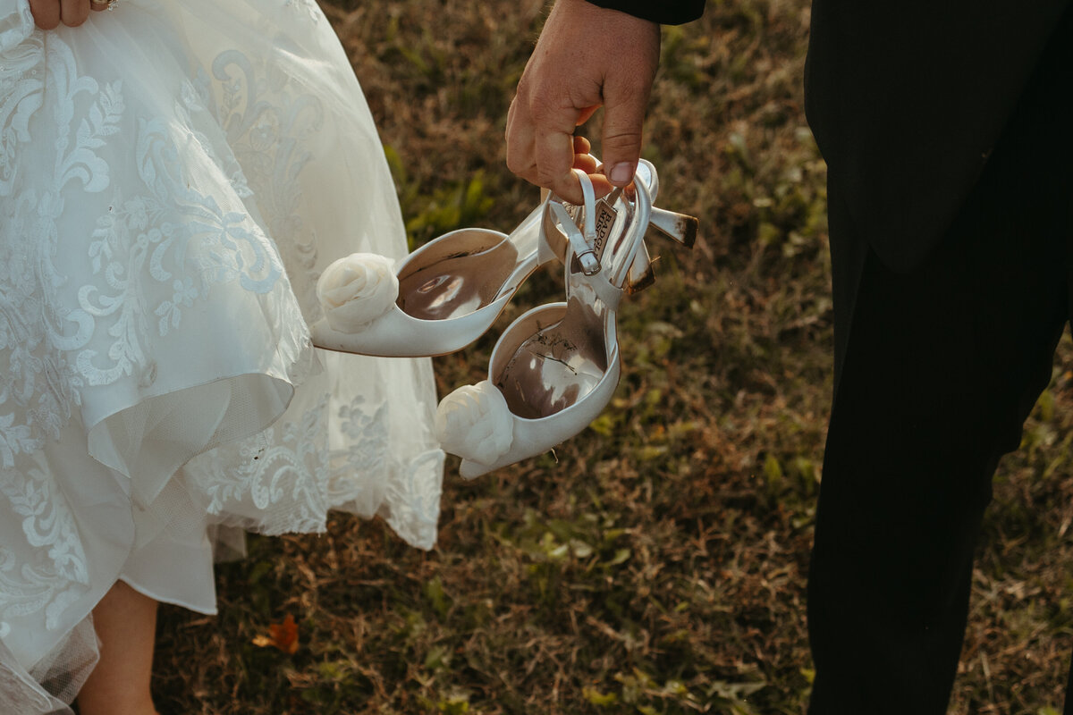 groom holds muddy bride shoes