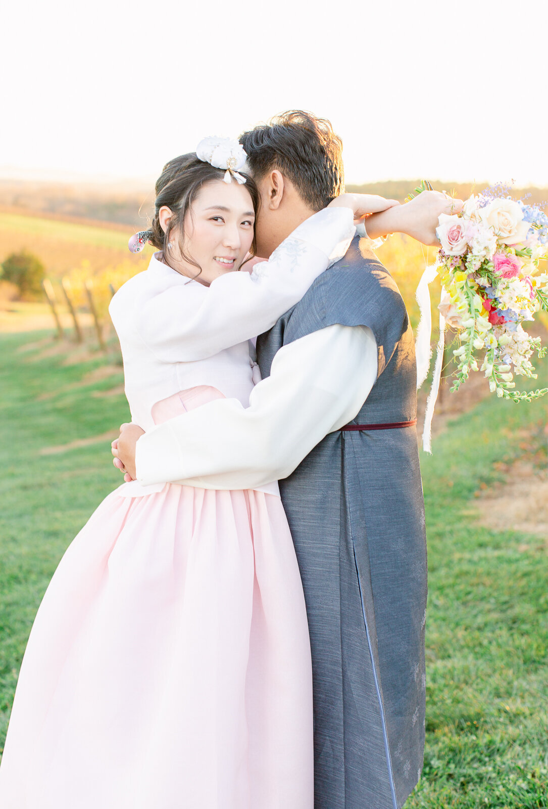 Korean bride with arms wrapped around her new husband's neck in the Vineyard at Stone Tower Winery. Captured by Bethany Aubre Photography.