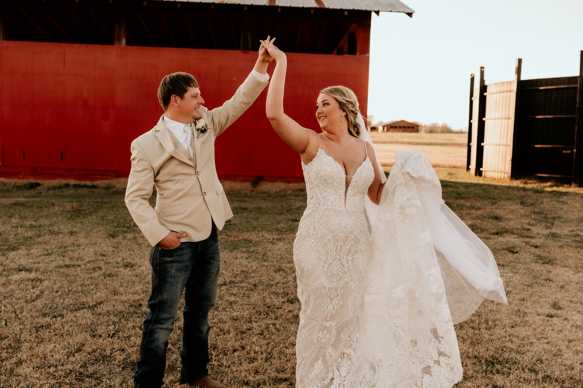 groom dancing with his bride during their outdoor bridal session as the bride holds her wedding dress train and the groom twirls her around in a circle