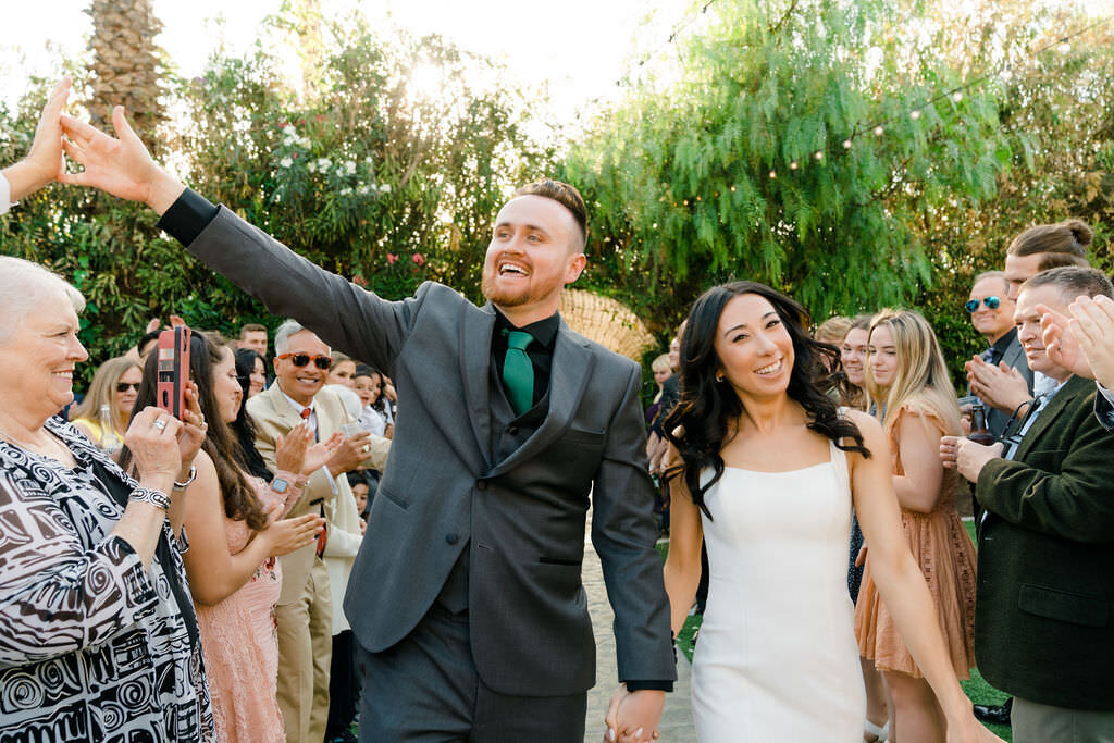 bride and groom holding hands and celebrating with guests as they walk back up the aisle