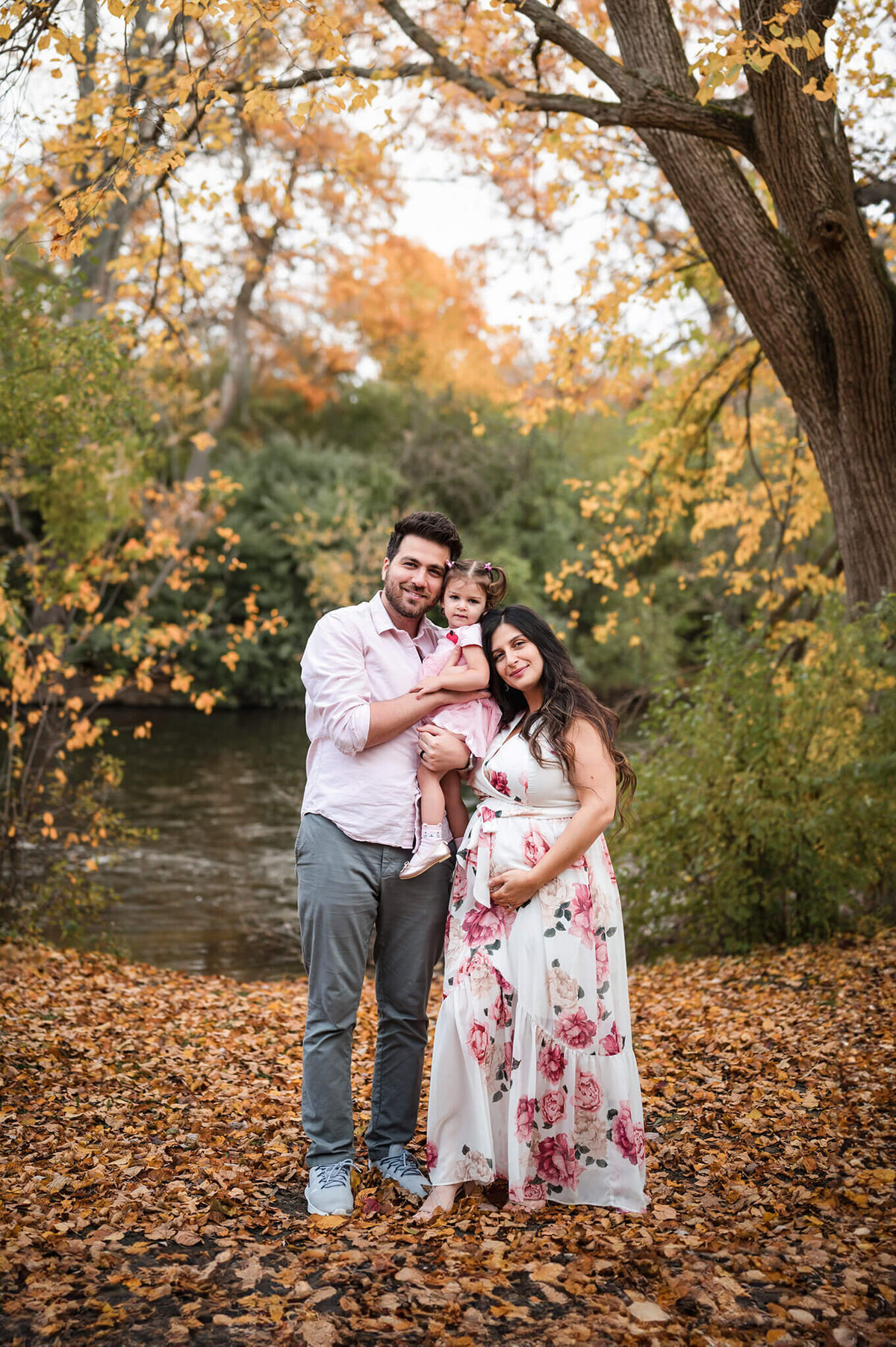 Family standing in fall foliage posing for maternity photos at Island Park in Ann Arbor