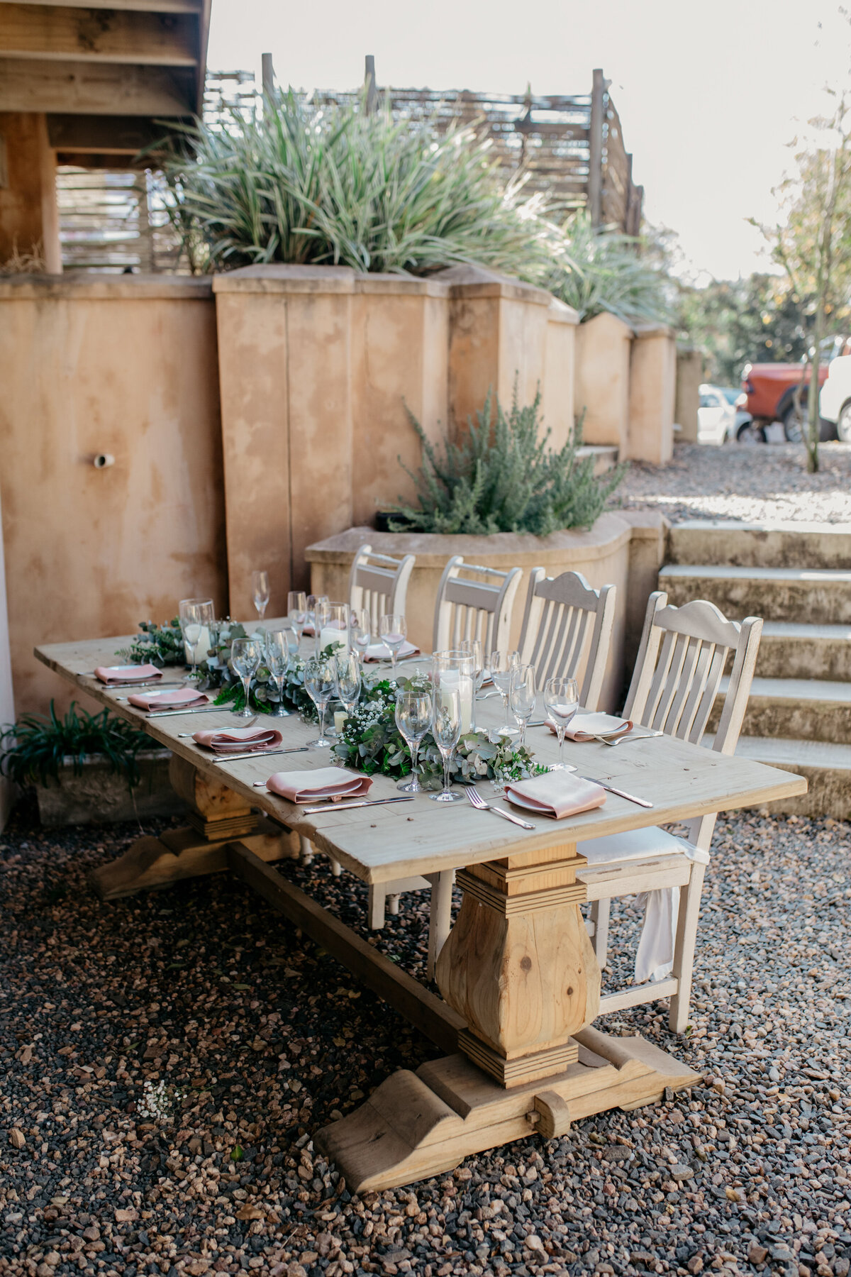 A reception setup with a wooden table and chairs, decorated with green florals. 