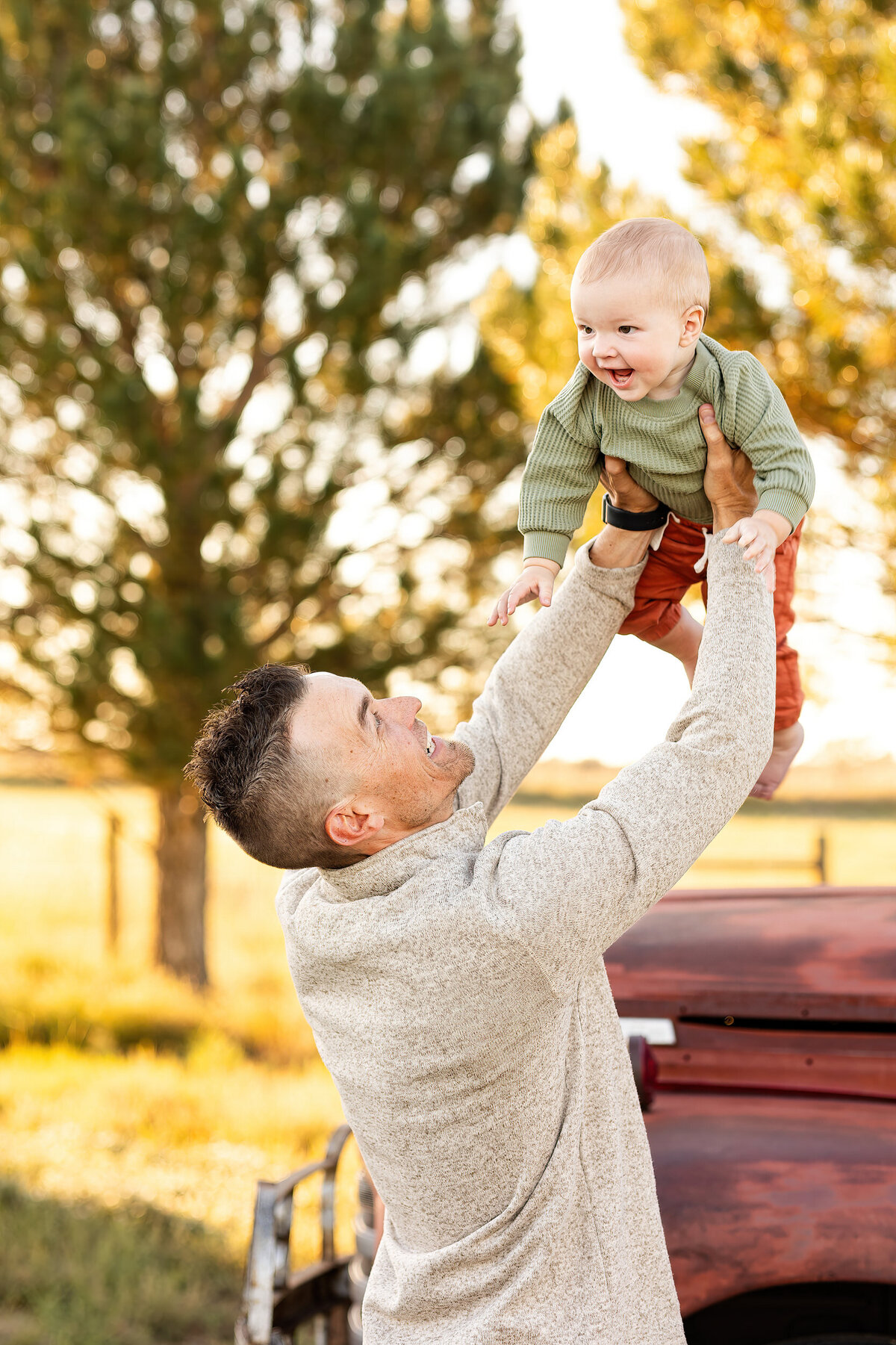 A dad holds his baby in the air while the baby laughs.