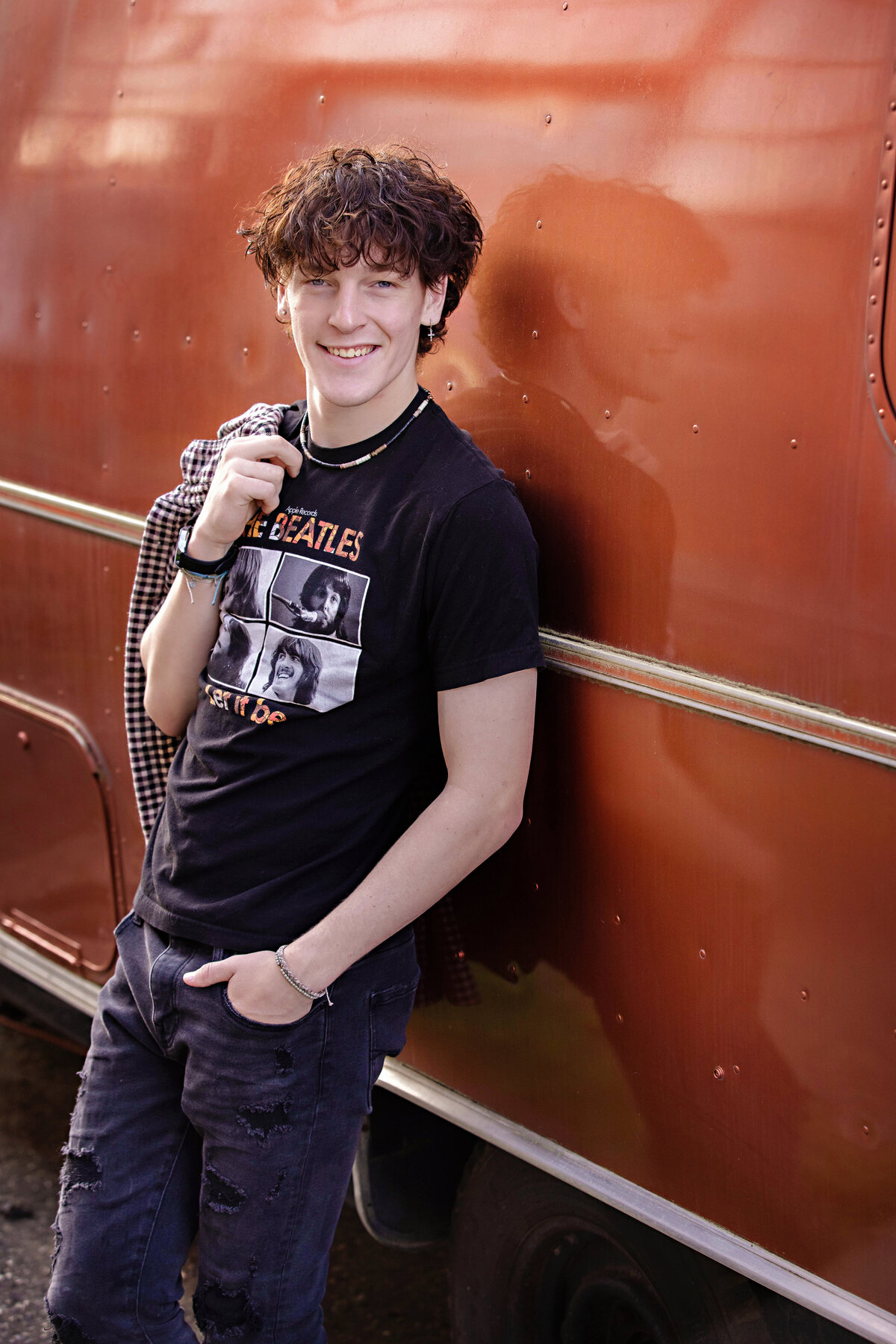 High school senior leaning on a vintage orange trailer wearing a band tee and layered spring outfit, photographed in Charlotte NC.