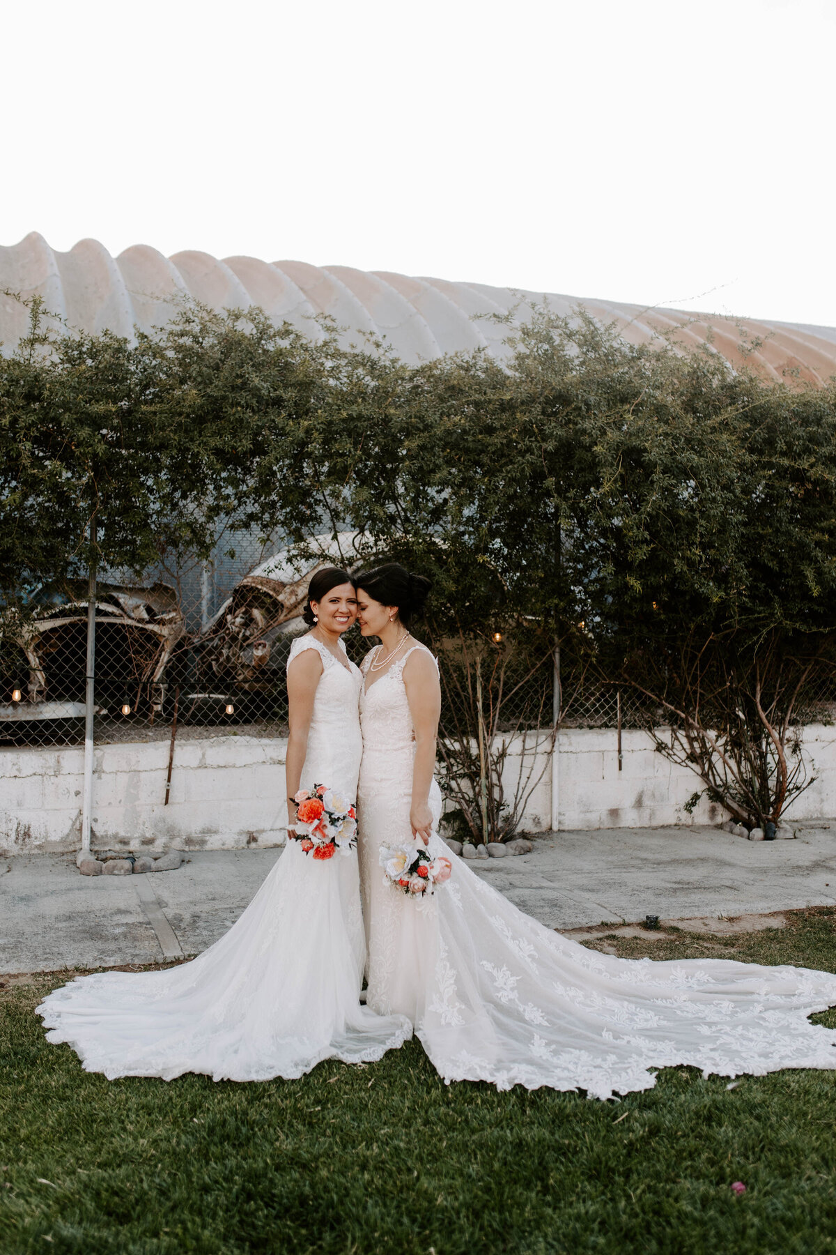 Two brides smile and hold one another on their wedding day.