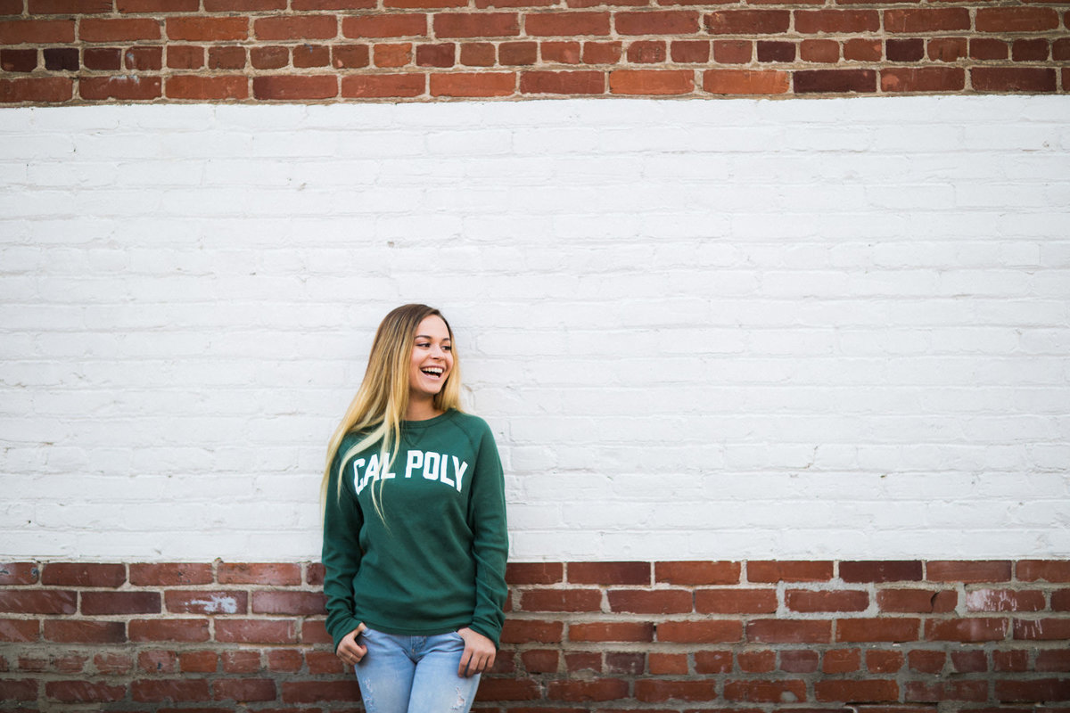 College senior leans back against a brick wall and smiles during her senior photos session
