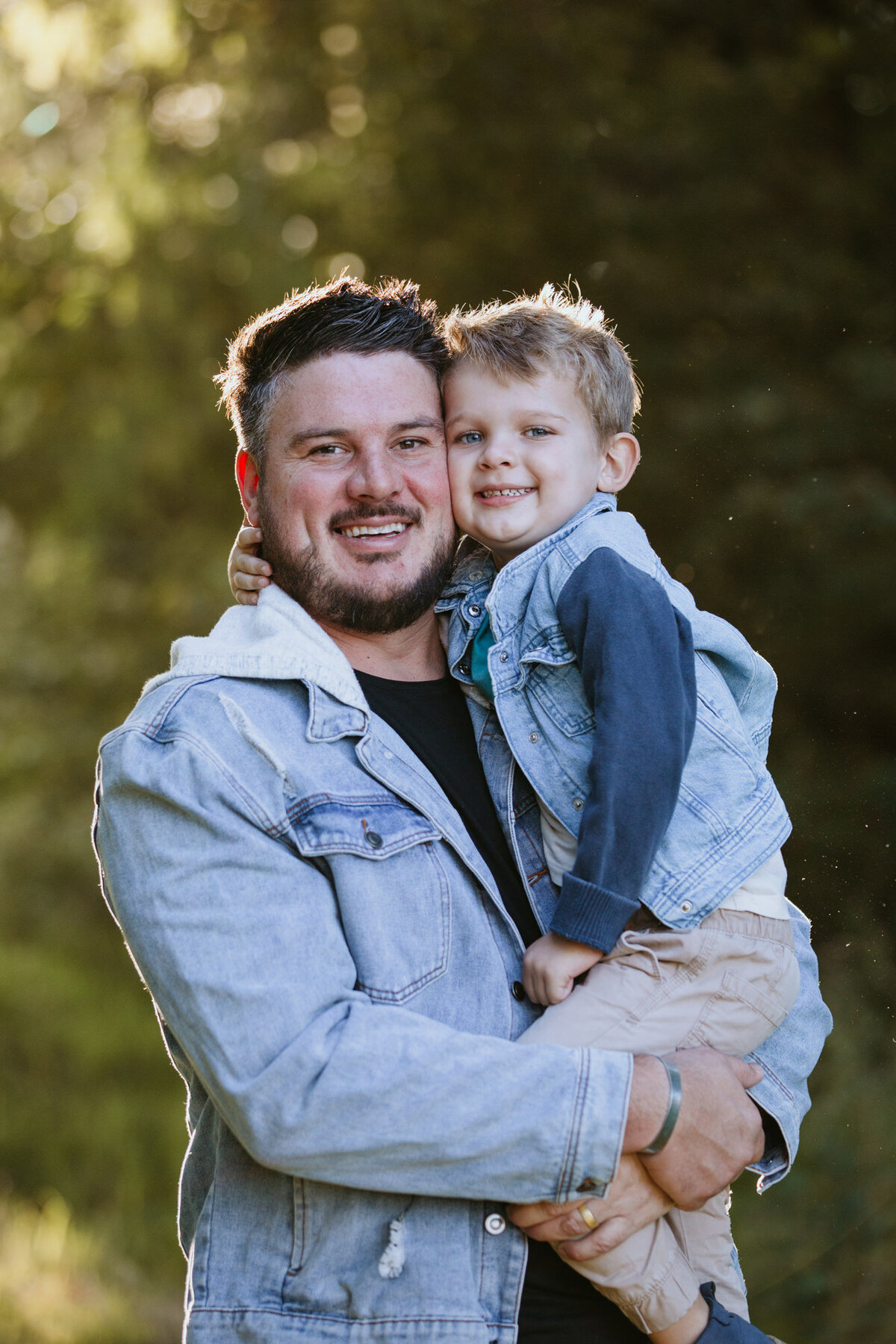 Father & Son sharing a cheek-to-cheek hug and smiling. 