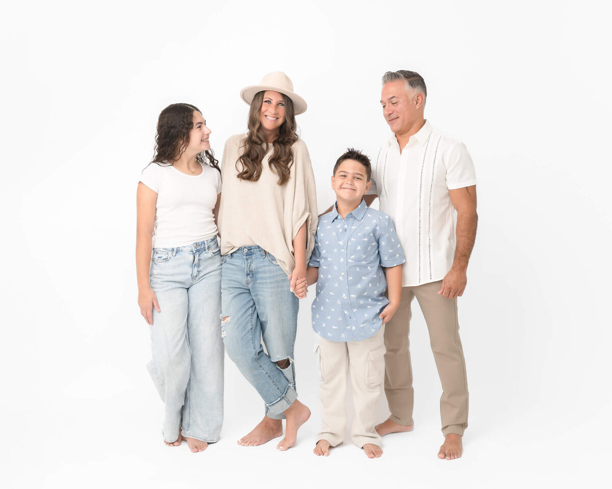 family with pre=teen girl and 8 year old boy dressed in light denim and neutrals in a white studio portrait