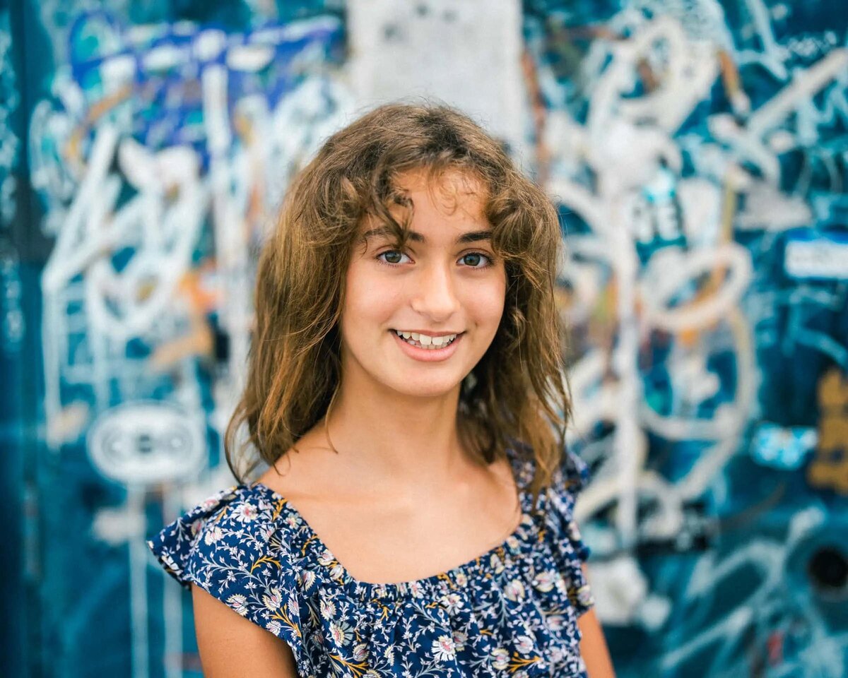 A young girl smiling in front of a graffitied wall