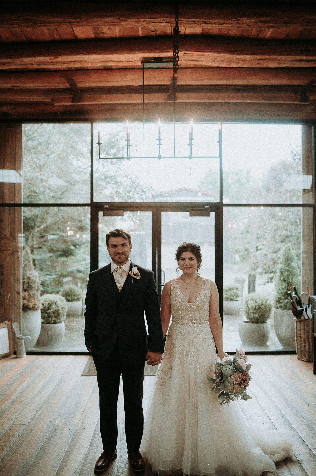 a bride and groom standing in the glass doorway with beautiful light behind them inside the Willowbrook wedding venue