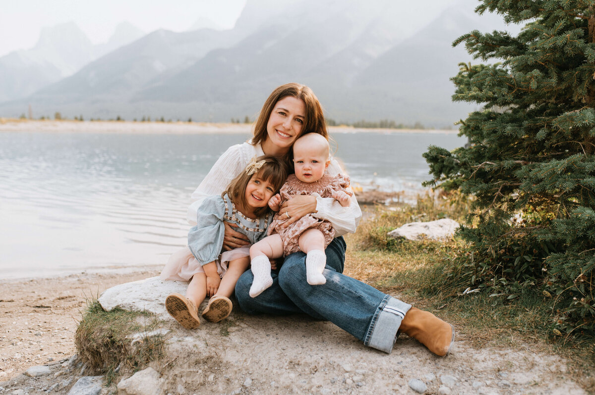 Mother-holding-2-children-in-front-of-mountains-and-water