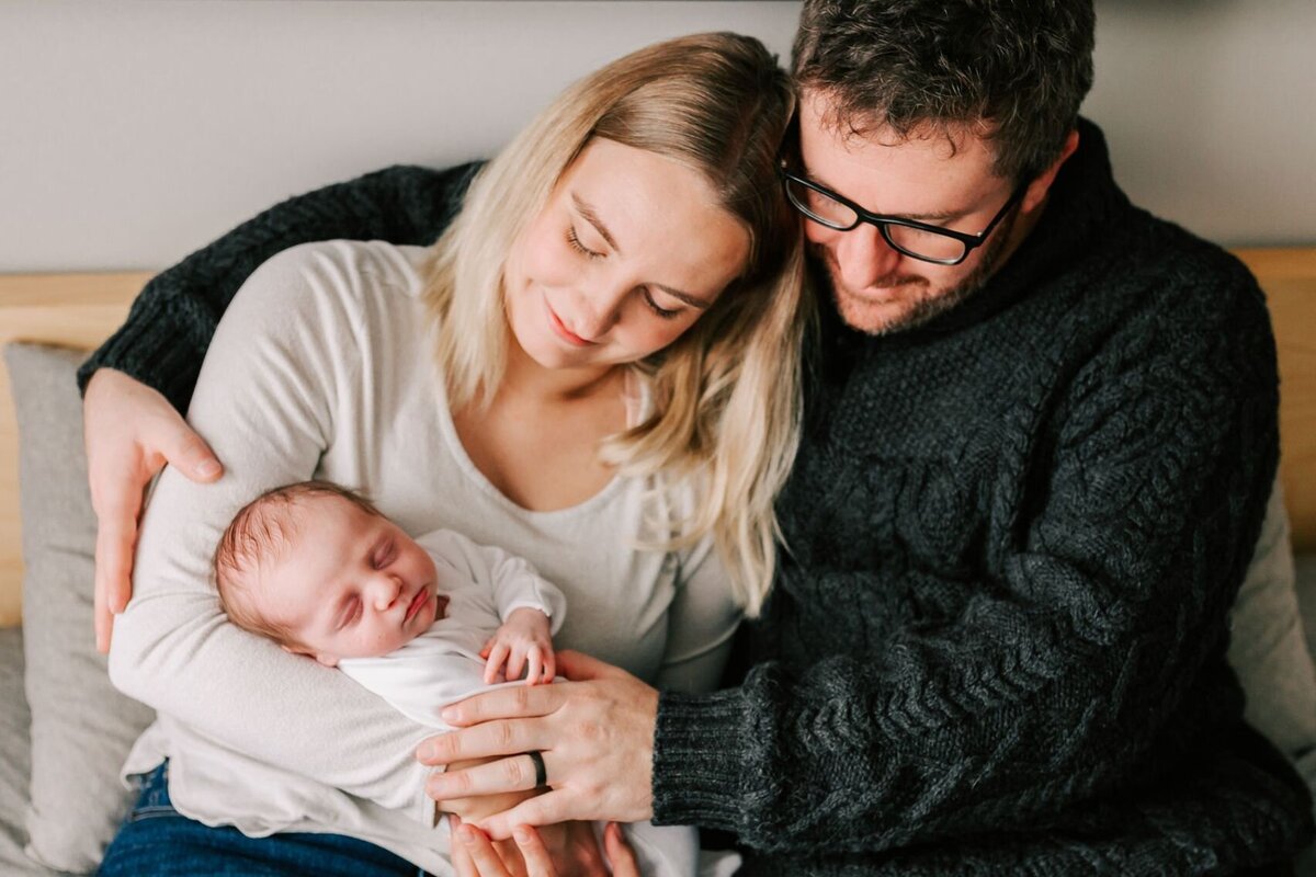 New parents snuggled baby on their bed during their lifestyle session