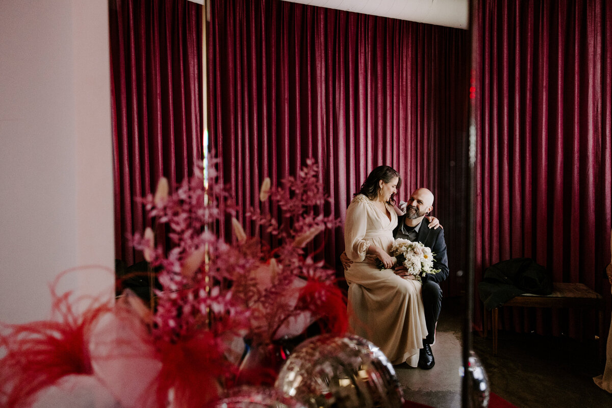 A bride sits on the groom's lap on their elopement day.