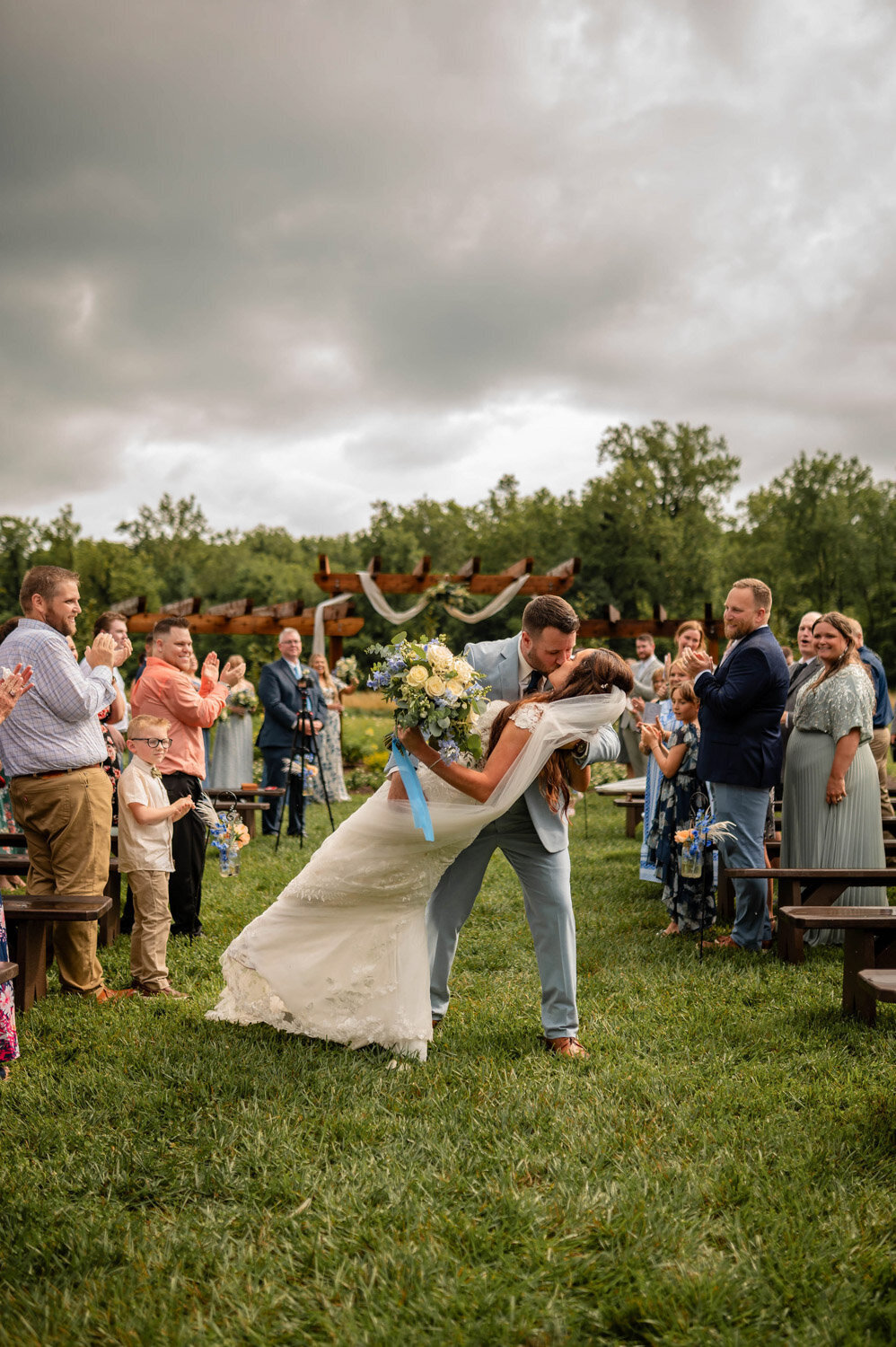Bride and groom share a dip kiss in front of cheering guests at the pergola ceremony site