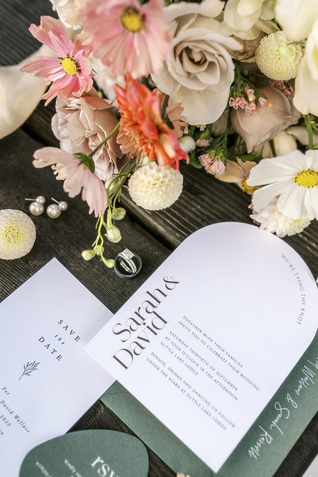 A wedding flat lay featuring invitations , flowers, and rings.