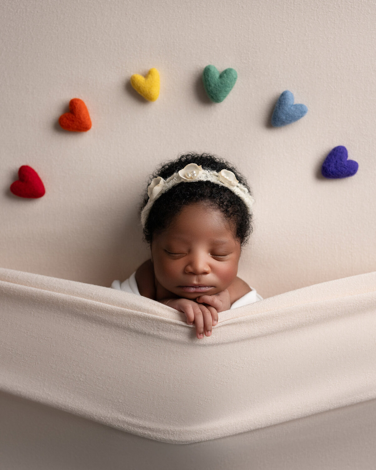 baby girl tucked into cream blanket with rainbow hearts overhead