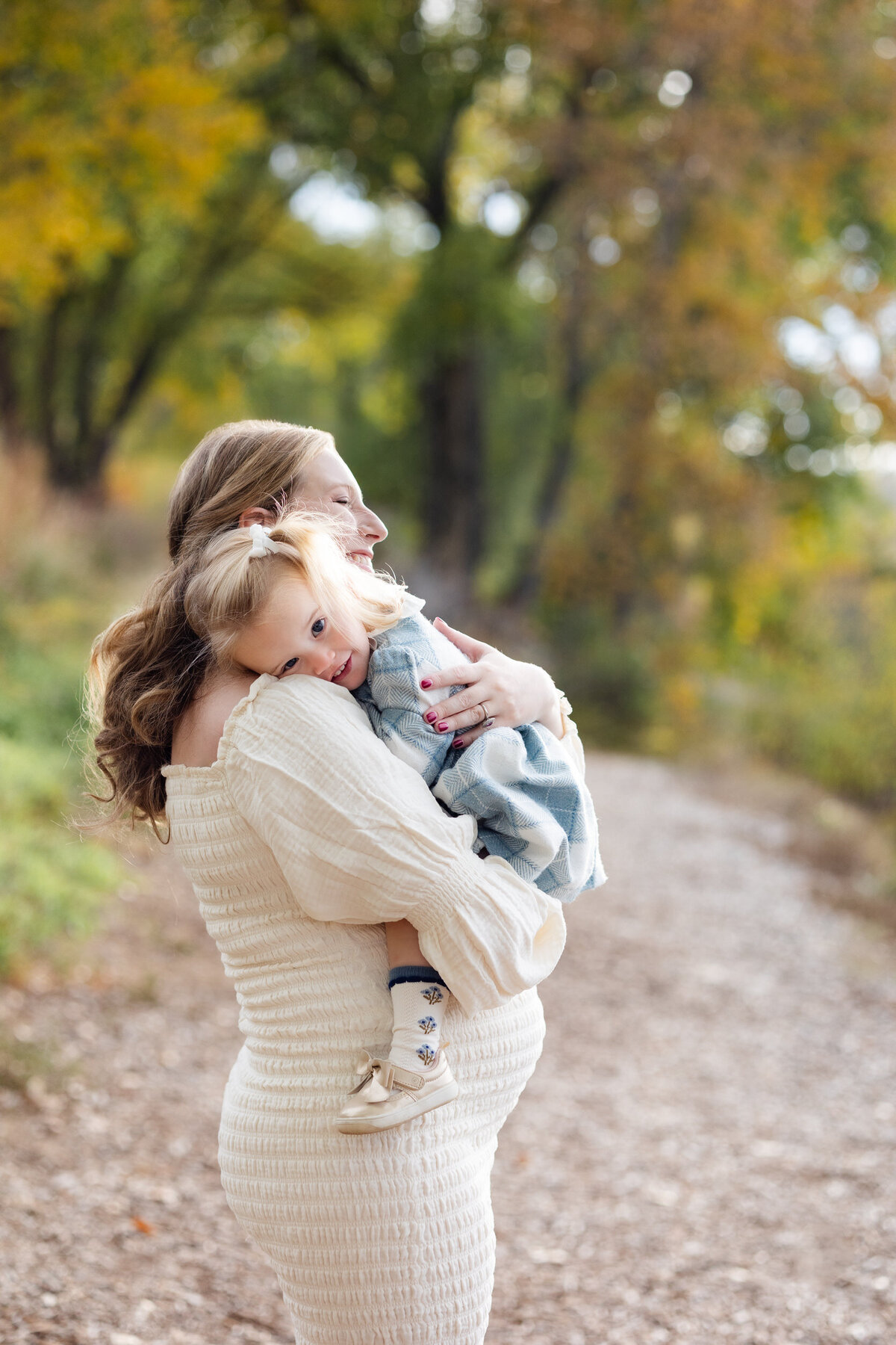 Toddler girl rests her head on her pregnant mom's shoulder as mom holds her.
