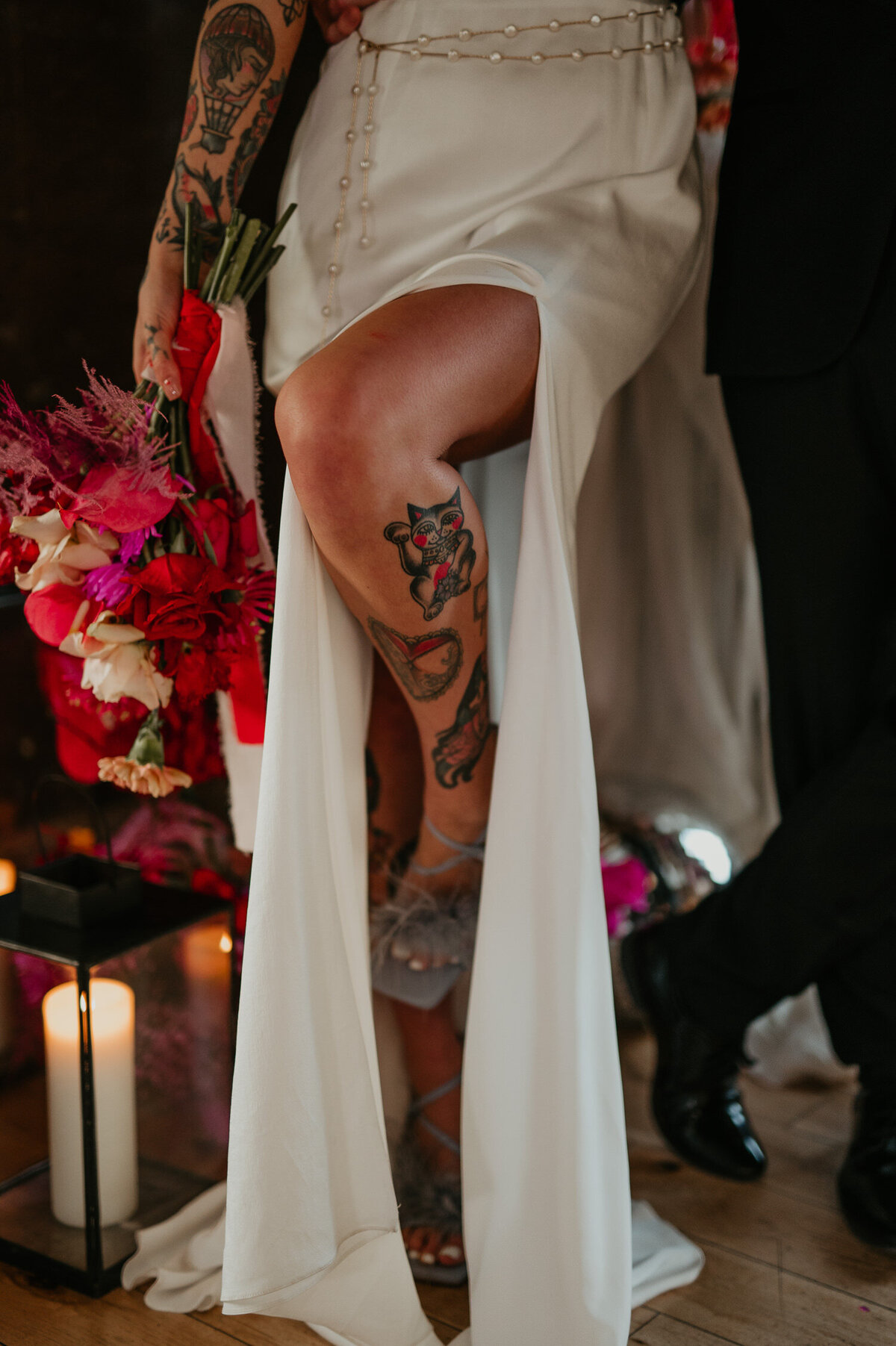 Details of a brides tattoos on her leg as they slip out of her wedding dress. She is holding a stunning pink bouquet.
