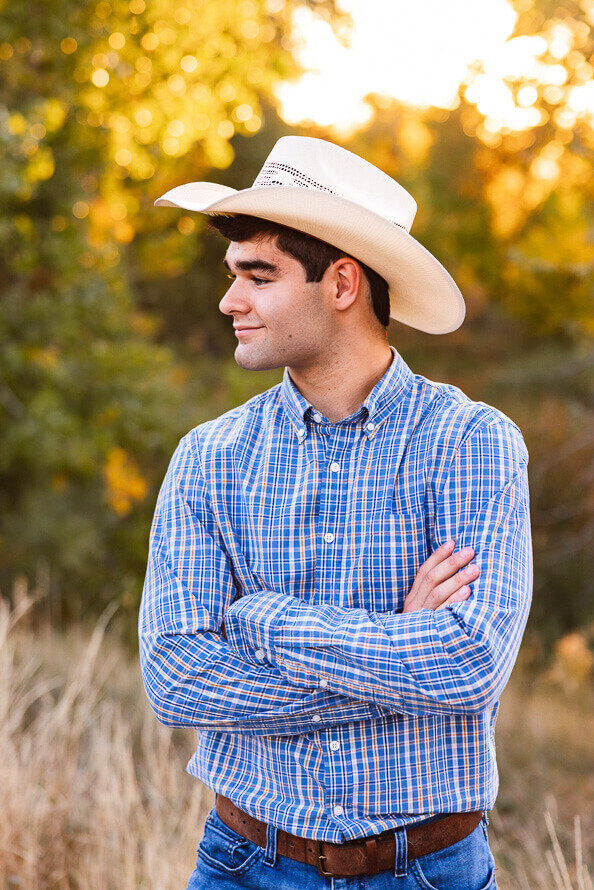 Senior boy with cowboy hat folds hands and looks off into the distance.