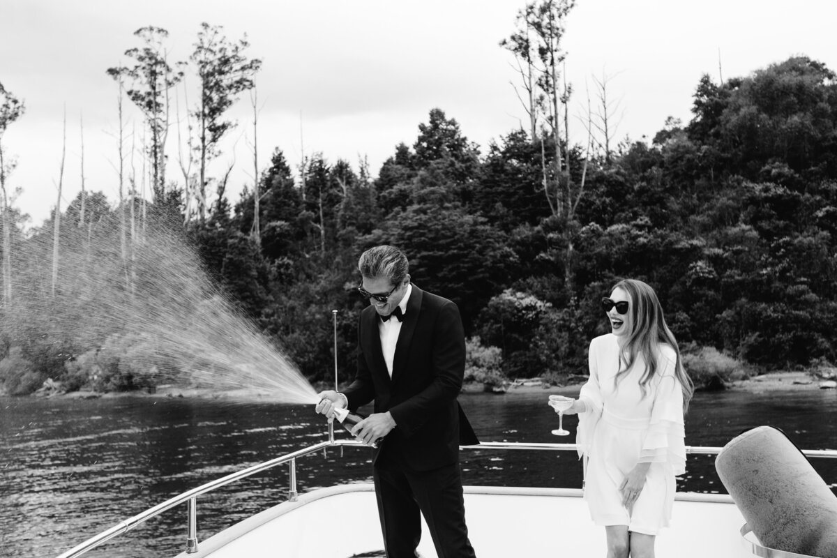 The Lovers Elopement Co - bride and groom laughing on back of boat on Queenstown lake