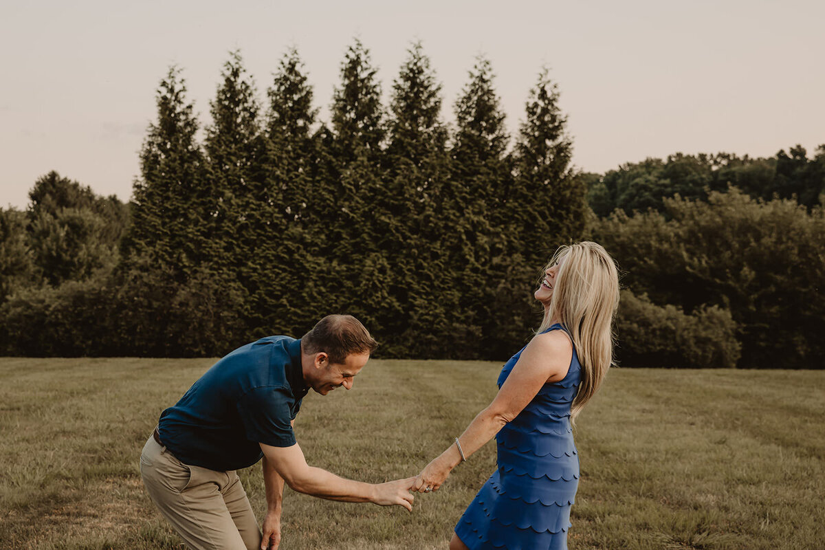 A couple holding hands in a field and laughing 