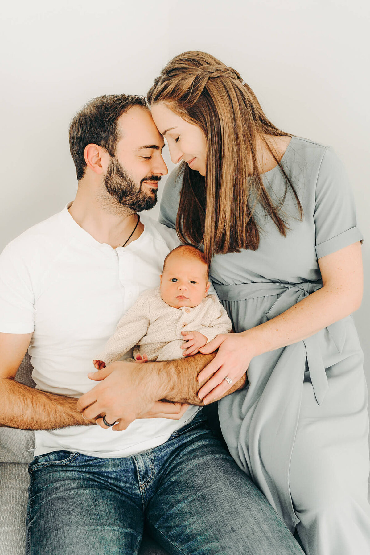 mom and dad snuggle while holding baby for newborn photos in jackson missouri