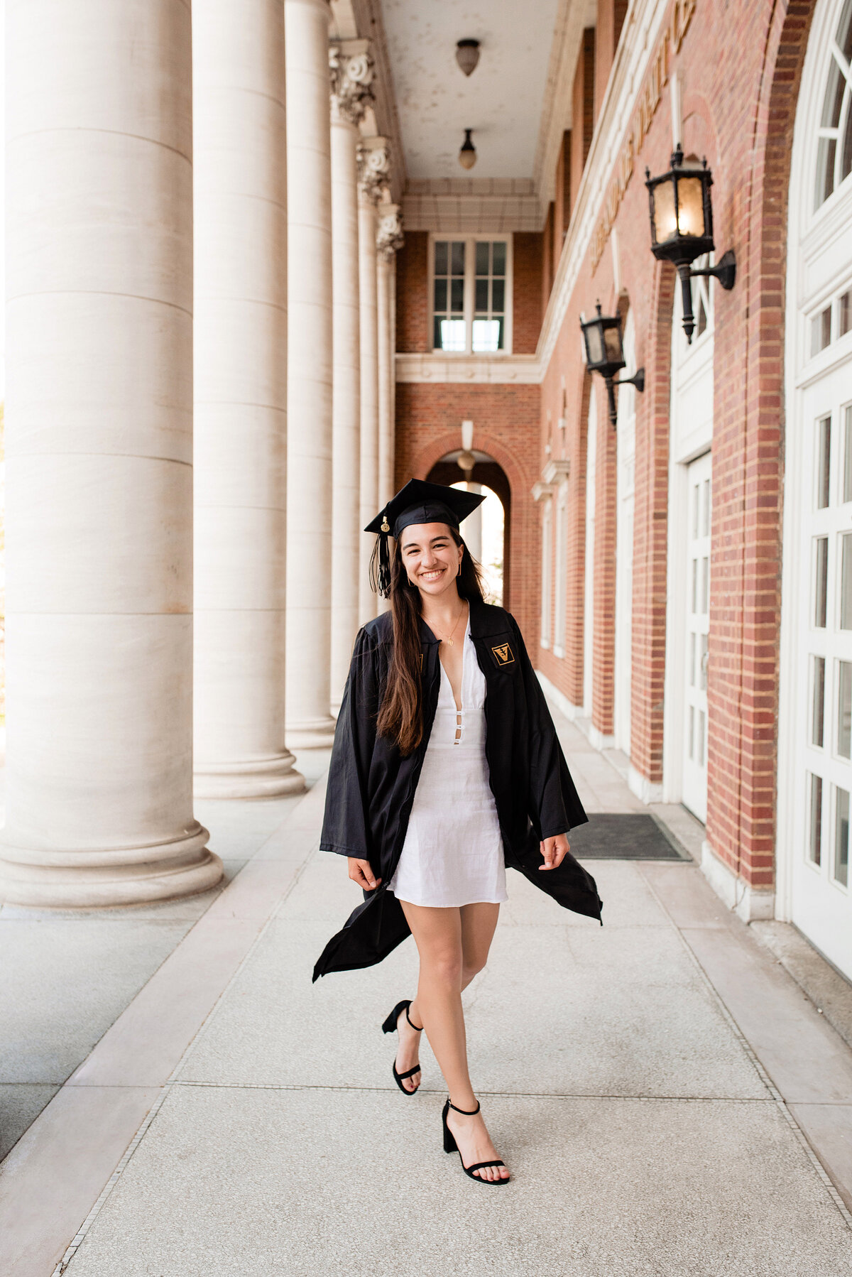 Girl wearing cap and gown for Vanderbilt graduation walking by pillars at Wyatt Center