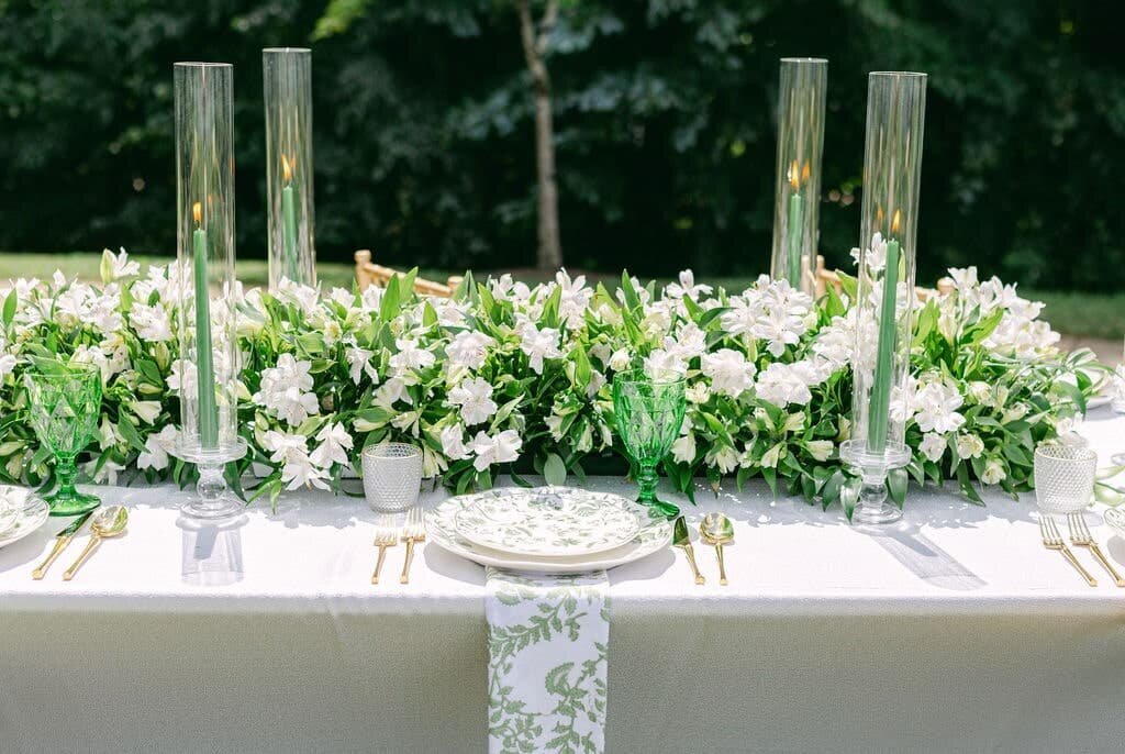 Lush green and white wedding reception table decor with a long floral runner and tall candles, designed by a leading Maryland wedding florist.