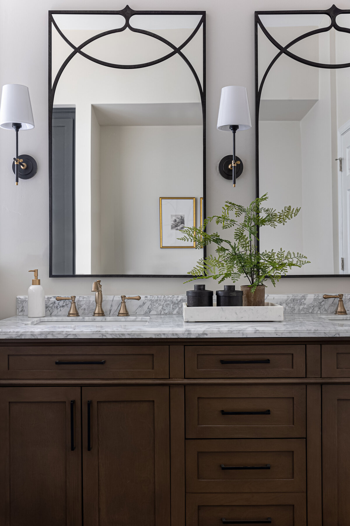 Simple neutral bathroom with statement mirrors, wood cabinets, and marble counter top.