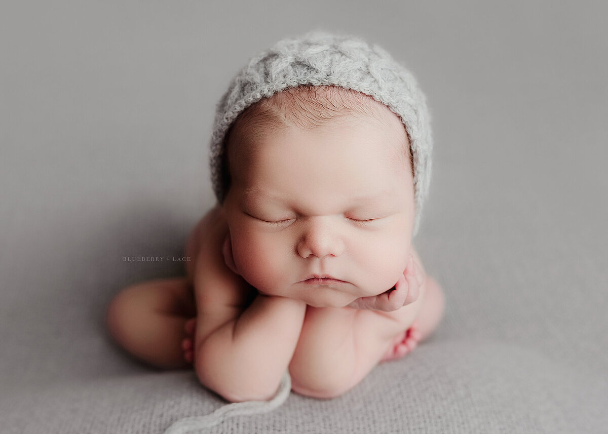 baby boy wearing a grey bonnet on a grey fabric in the froggy pose