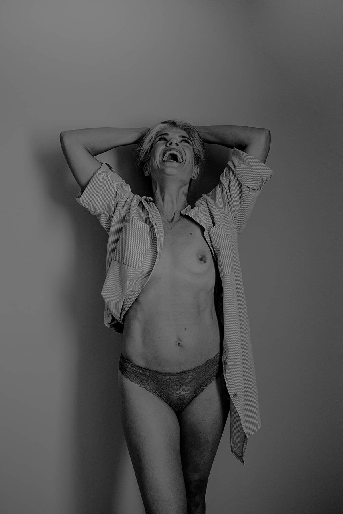 En naken kvinne som står foran en vegg og ler høyt.