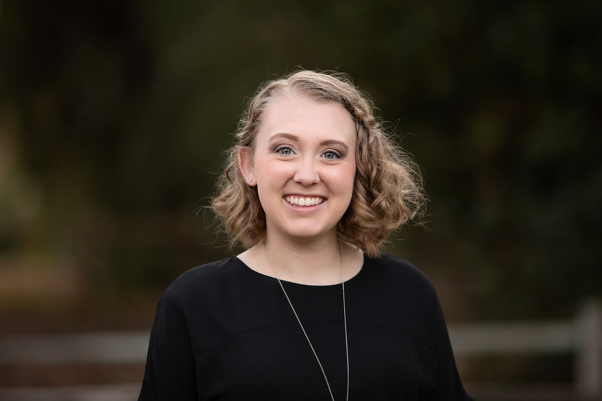 A smiling woman in a black top, captured outdoors in a family photography session by a family photographer.