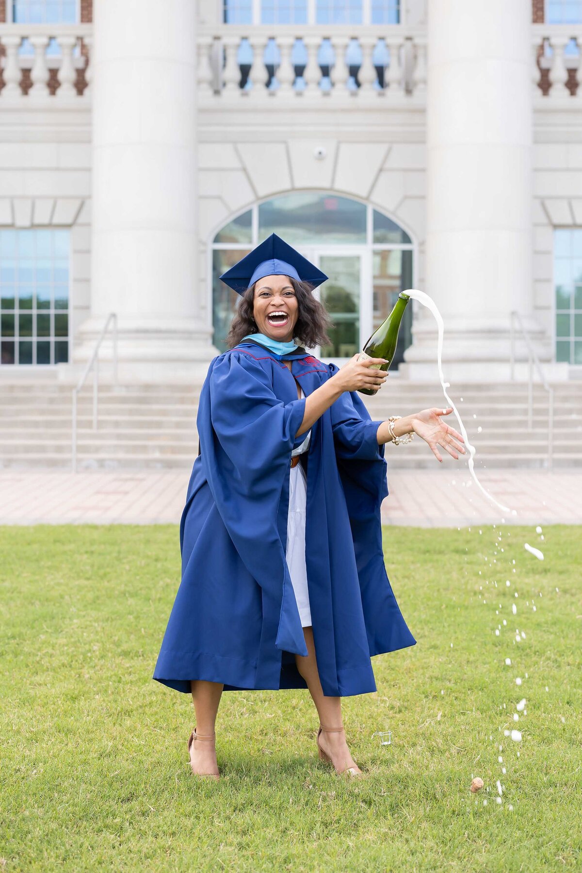 Senior Photography Portfolio featuring a joyful female university graduate celebrating with champagne, dressed in a blue cap and gown.