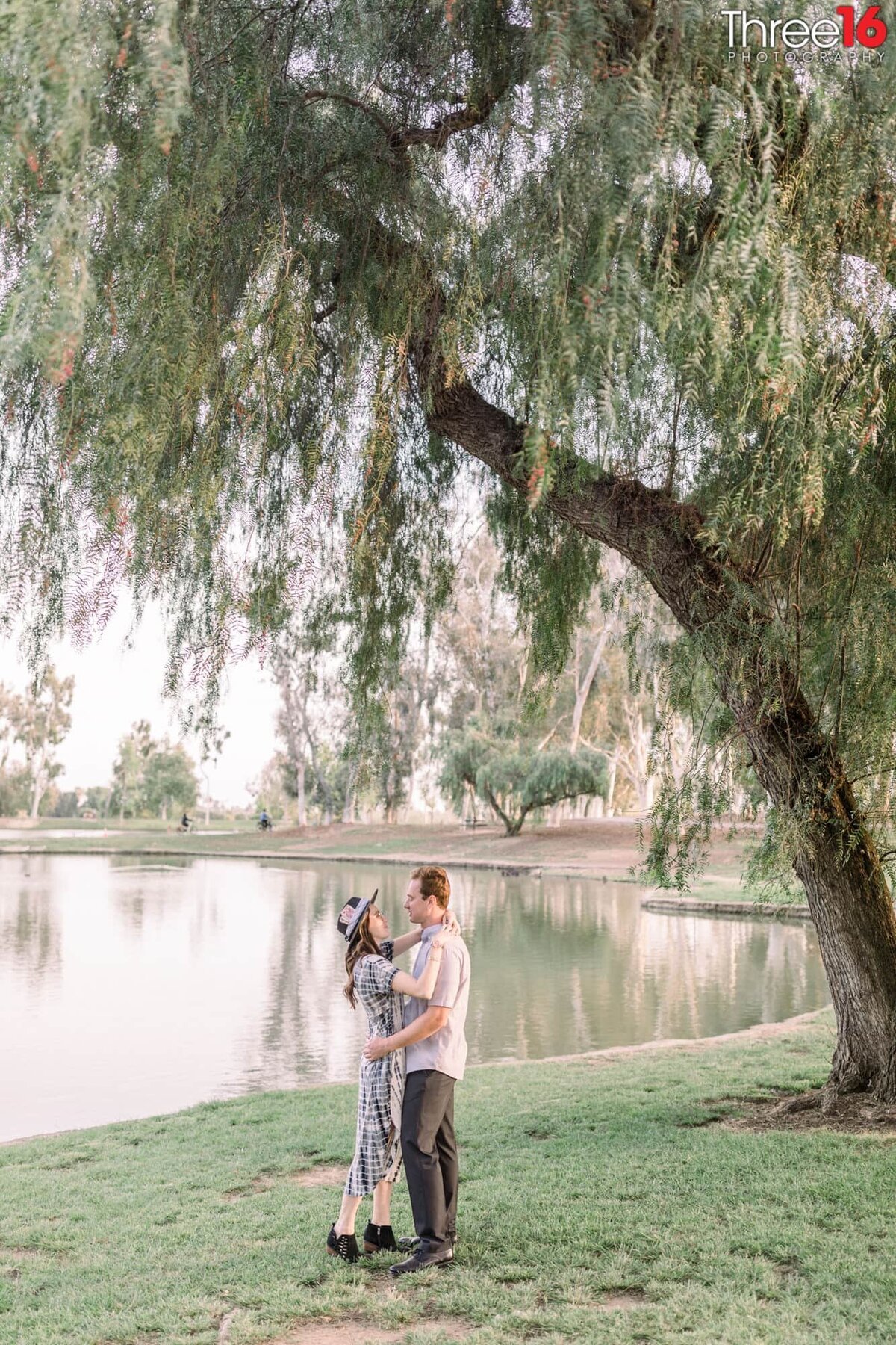Tender moment for engaged couple with Tri-City Park lake behind them