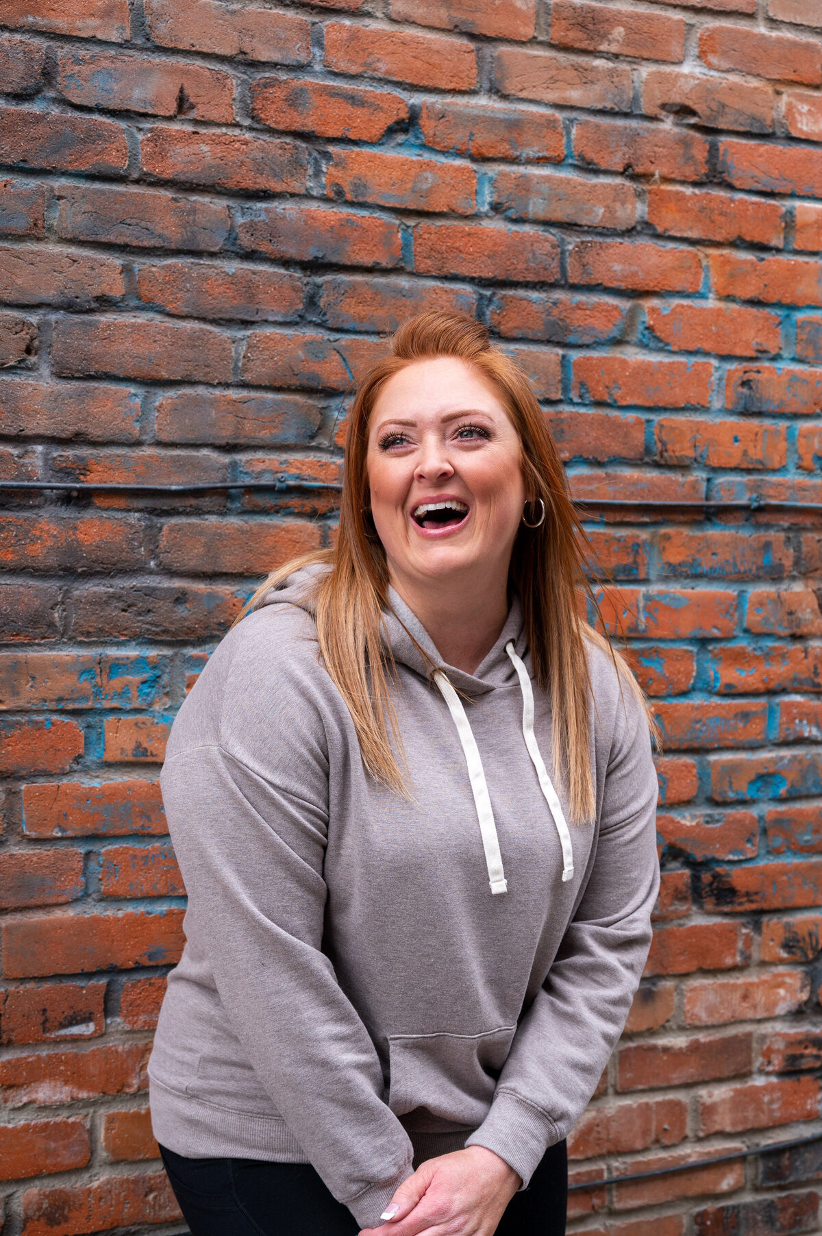 woman with red hair leaning against brick building with gray hoodie