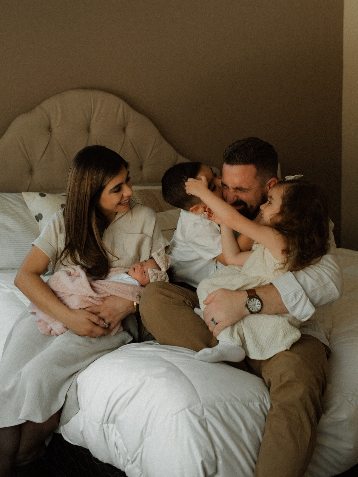 Parents snuggled on a bed with their three young children during an in-home newborn session in Southern California, capturing warmth, connection, and new beginnings.