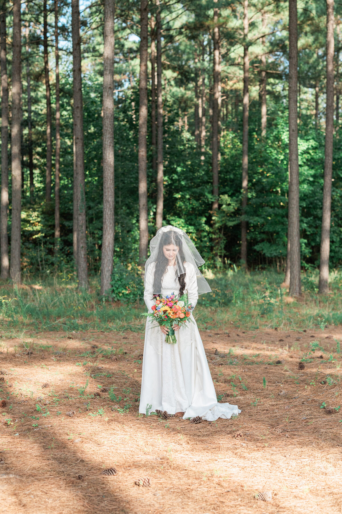 A bride standing in a wooded area holding a bouquet of flowers