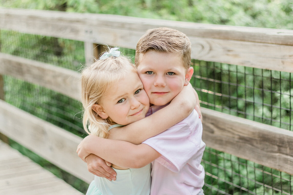 little brother and sister hugging on a bridge