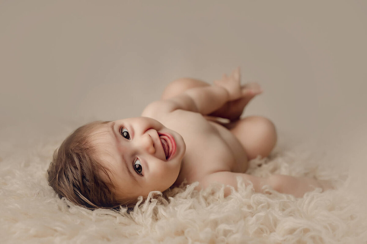 a six month old boy laying on his back holding his feet laughing at the camera