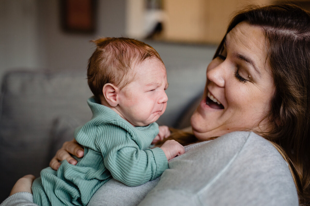 a new mom holds her baby while she's sitting on the couch.