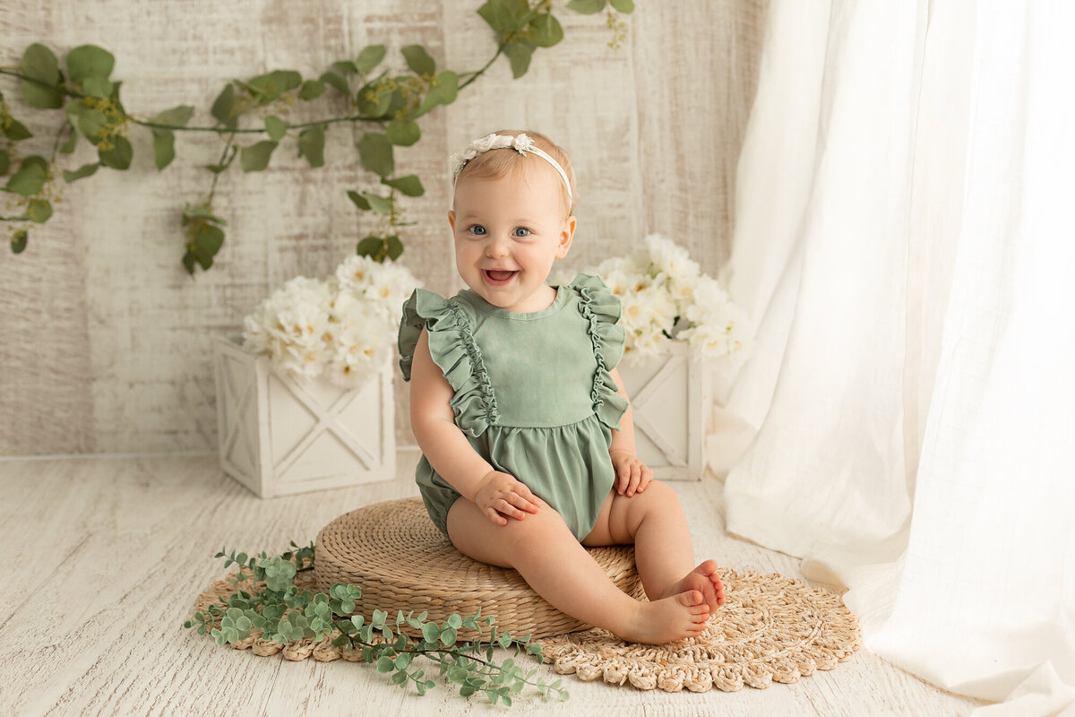 1 year old sitting up with white and green backdrop scene