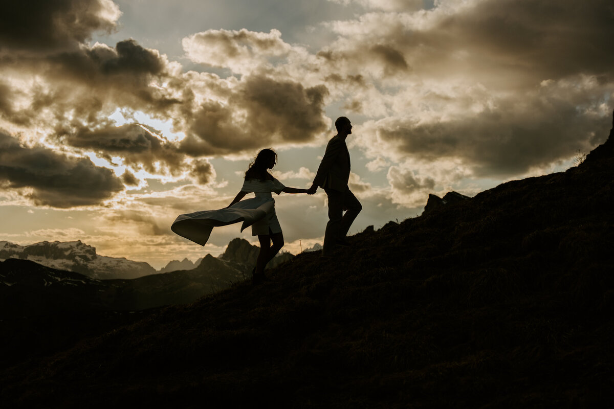 Silhouette of bride and groom holding hands on mountain ridge