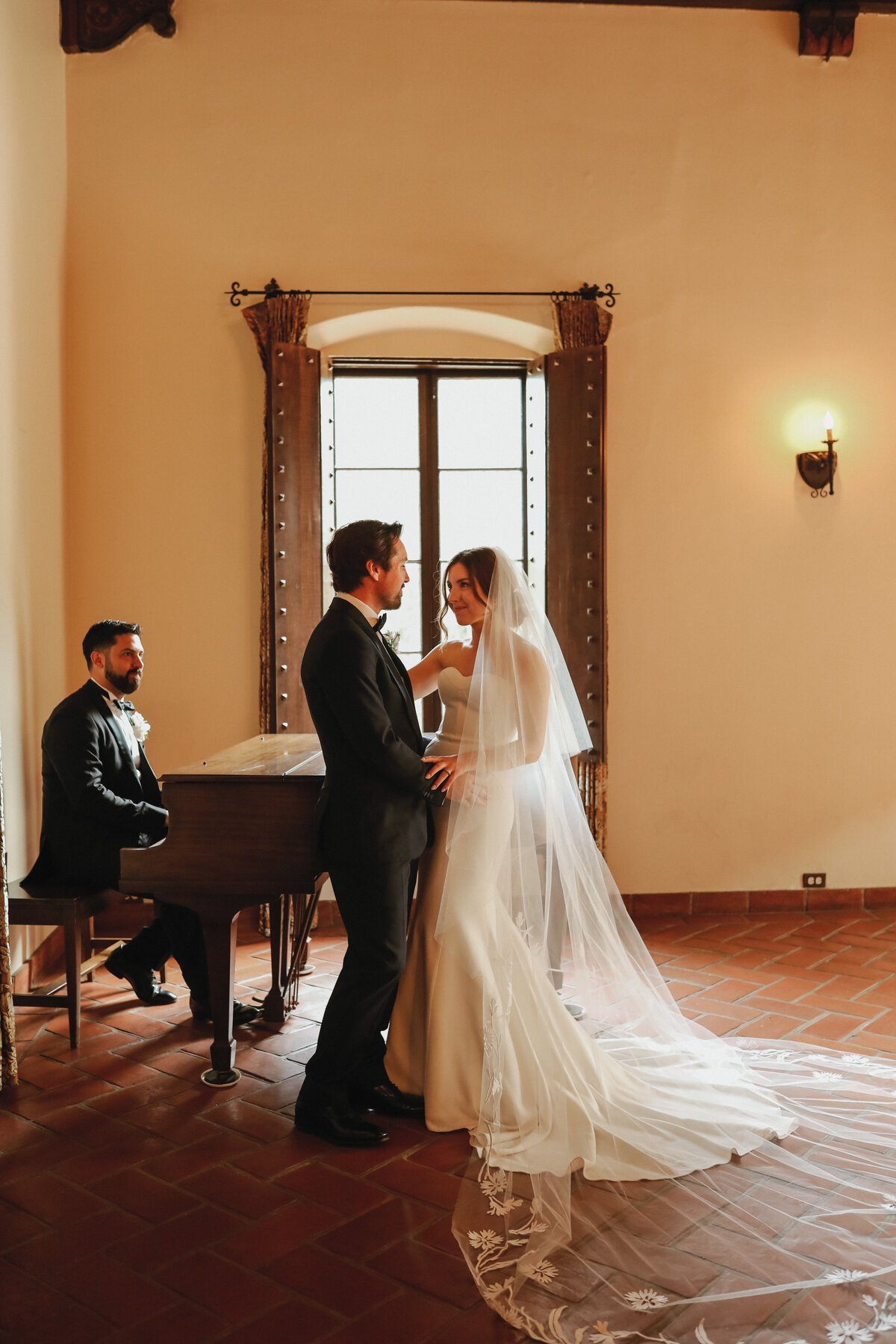 bride and groom standing against grand piano while groomsmen plays them a song